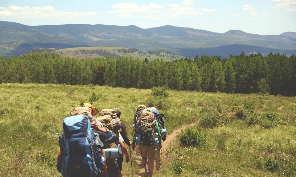 Un grup de joves d'excursió per un prat, carregant motxilles, en el marc d'una activitat d'educació en el lleure