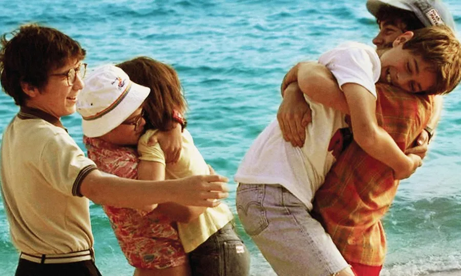 Una colla d'amics i amigues jugant i abraçant-se a la platja durant les vacances d'estiu
