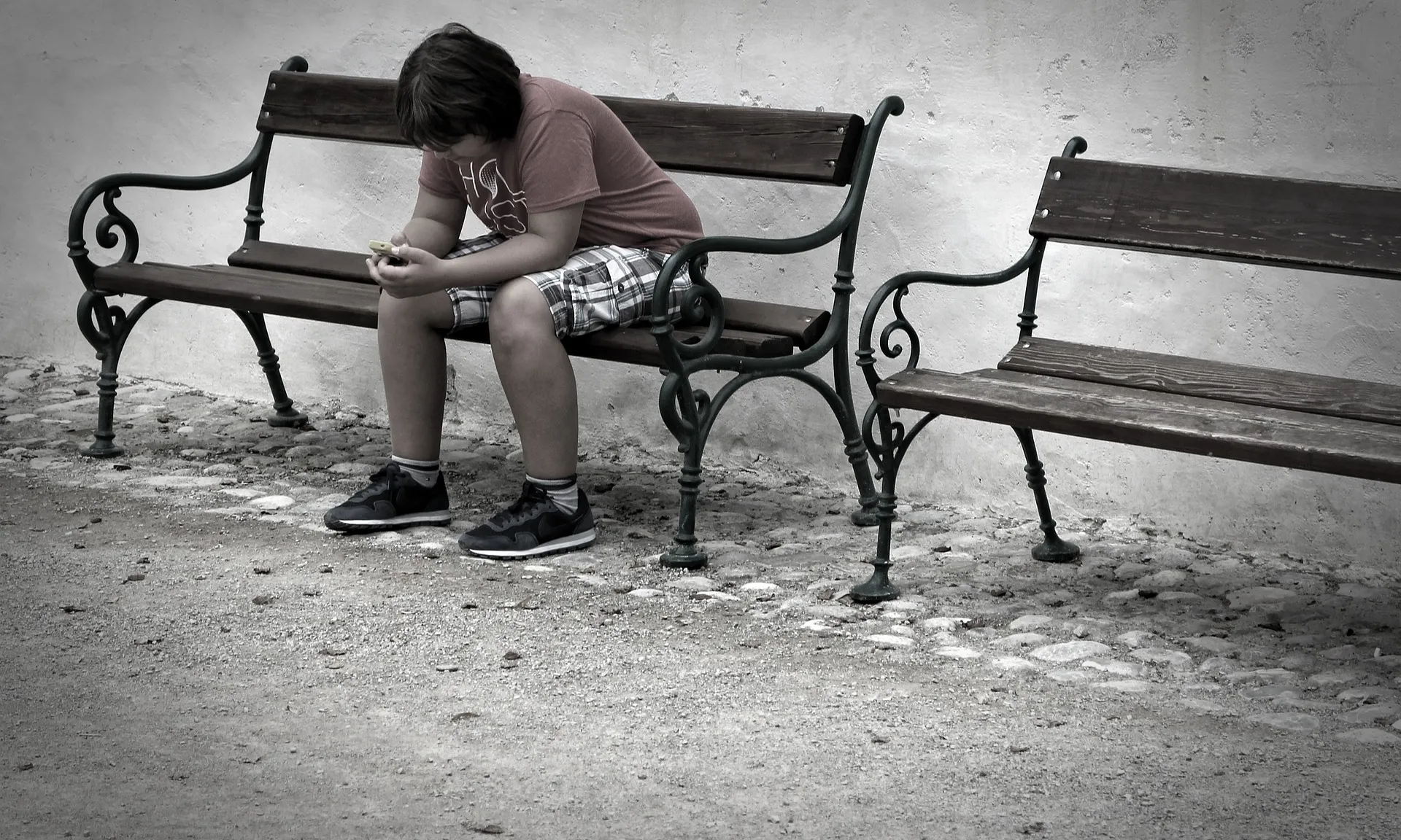 jove adolescent mirant el mòbil assegut en un banc de fusta