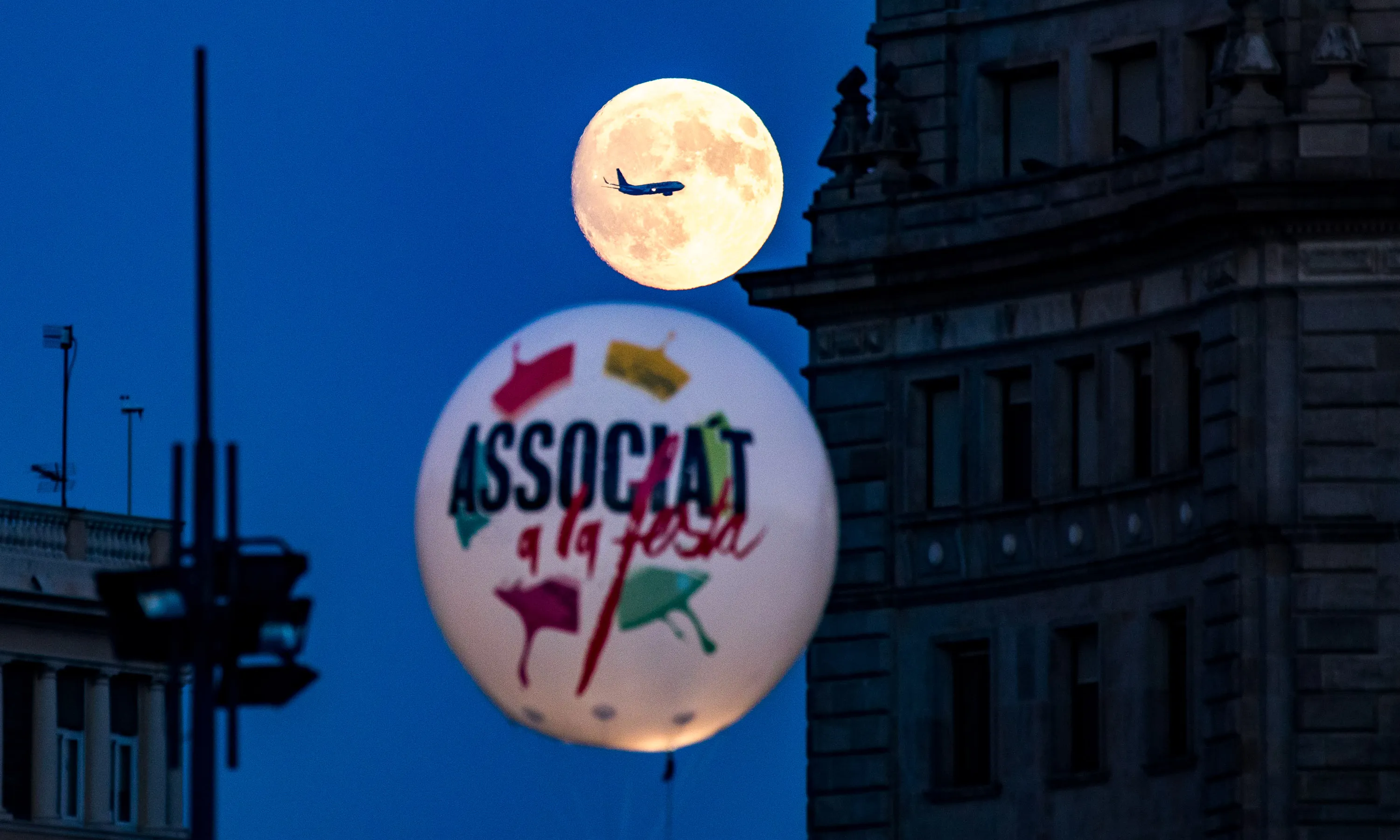 Globus de l'Associa't i de fons la lluna amb un avió que hi passa per davant