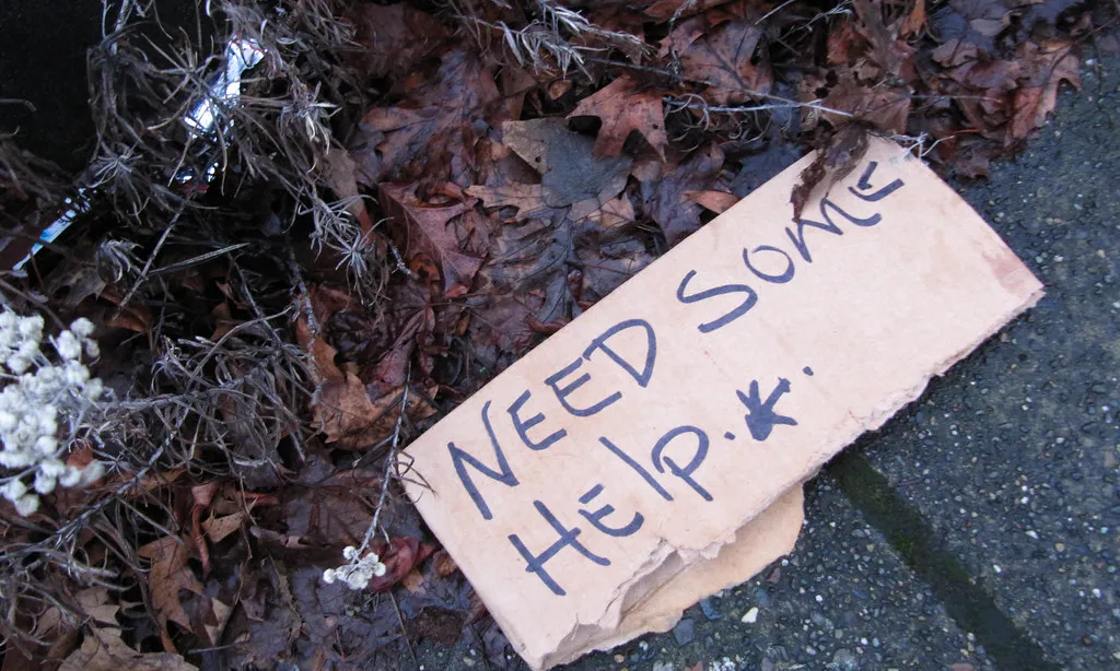 Cartró al terra en una vorera en què hi figura 'I need some help'