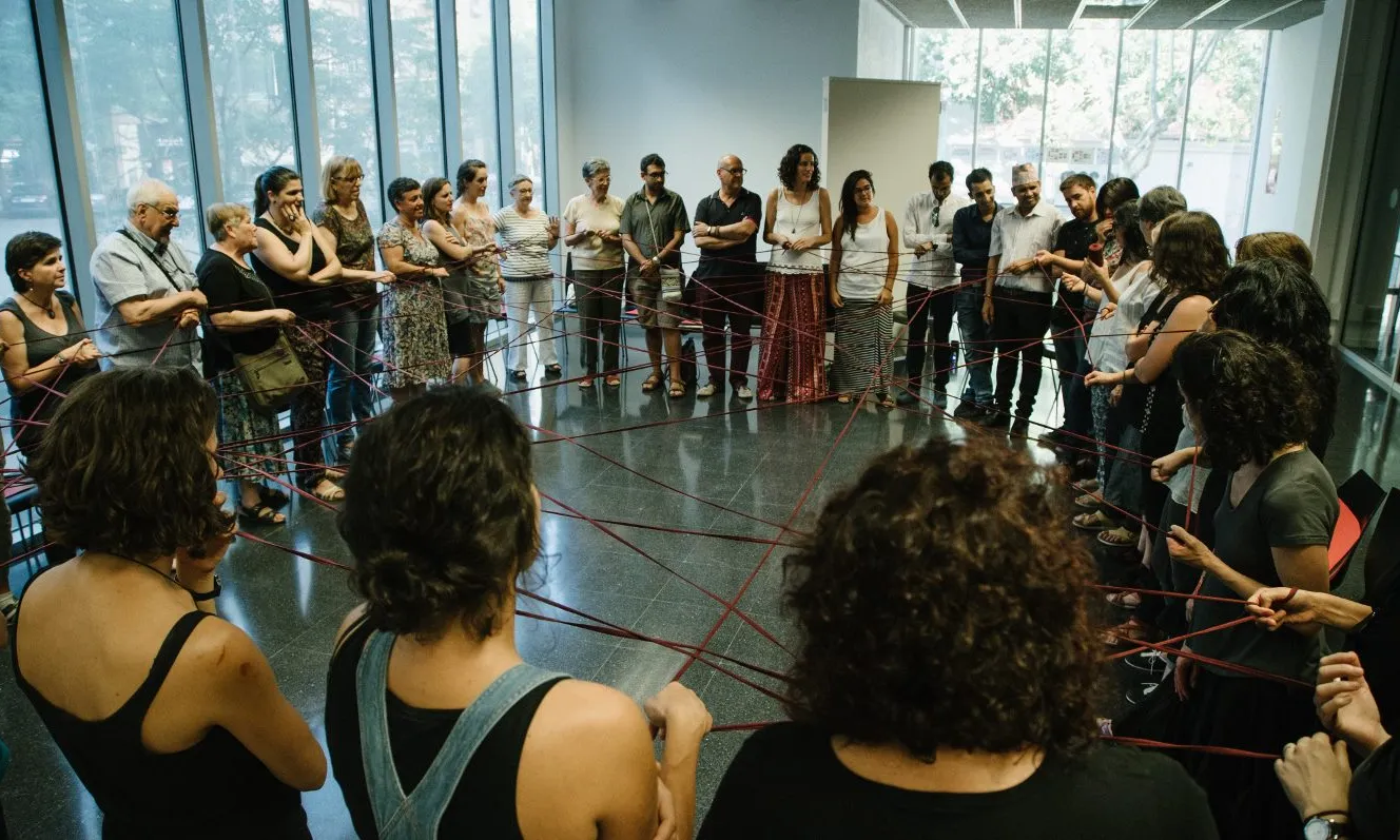 Un grup gran de gent participant en una dinàmica que els entrellaça amb una troca de llana