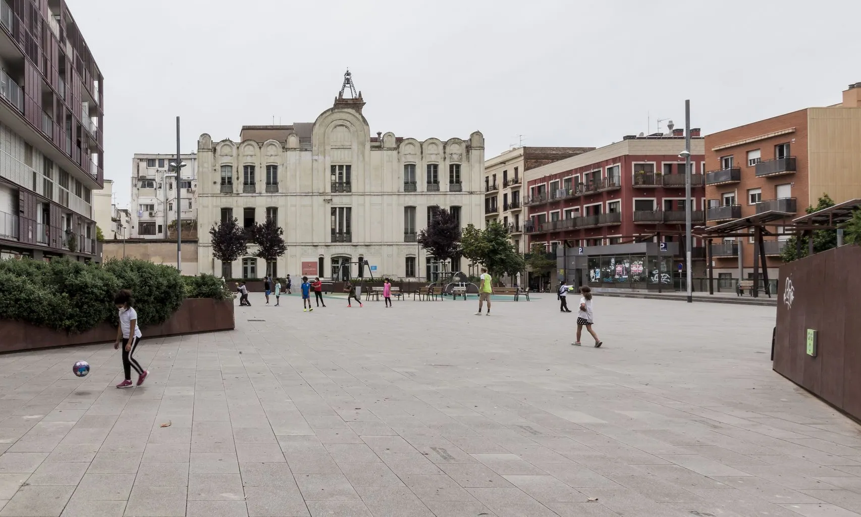 Vista general de la plaça de Joan Pelegrí amb nens jugant i l’Institut Escola Arts al fons.