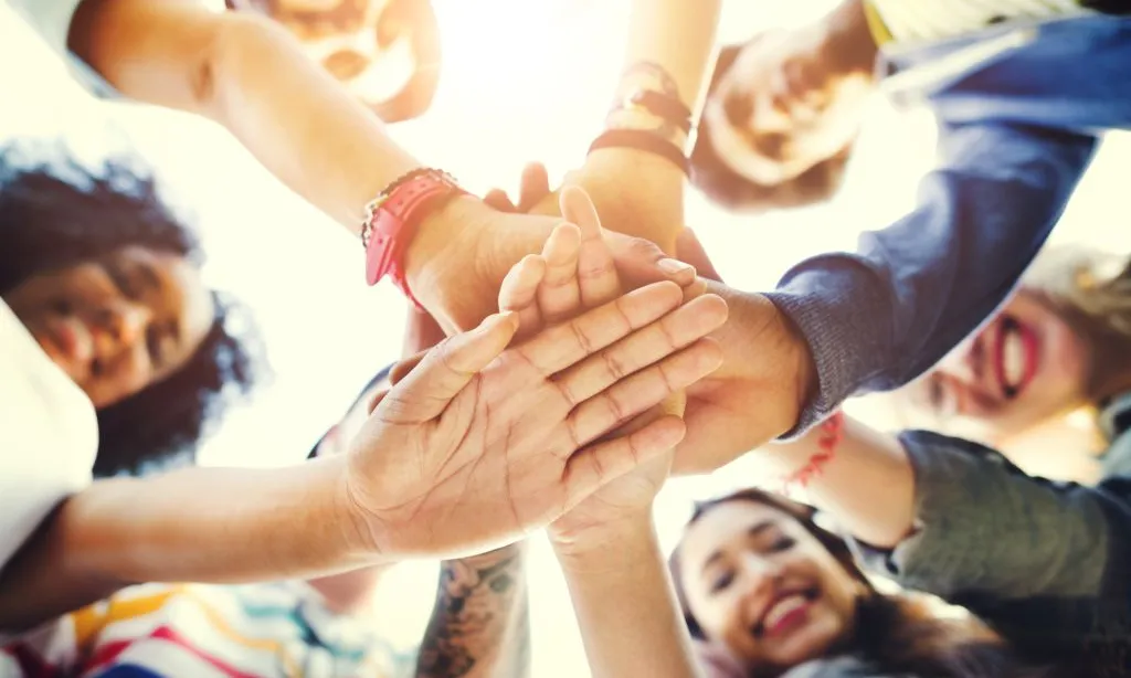Joves sumen forces per a treballar plegades, posant les mans juntes.