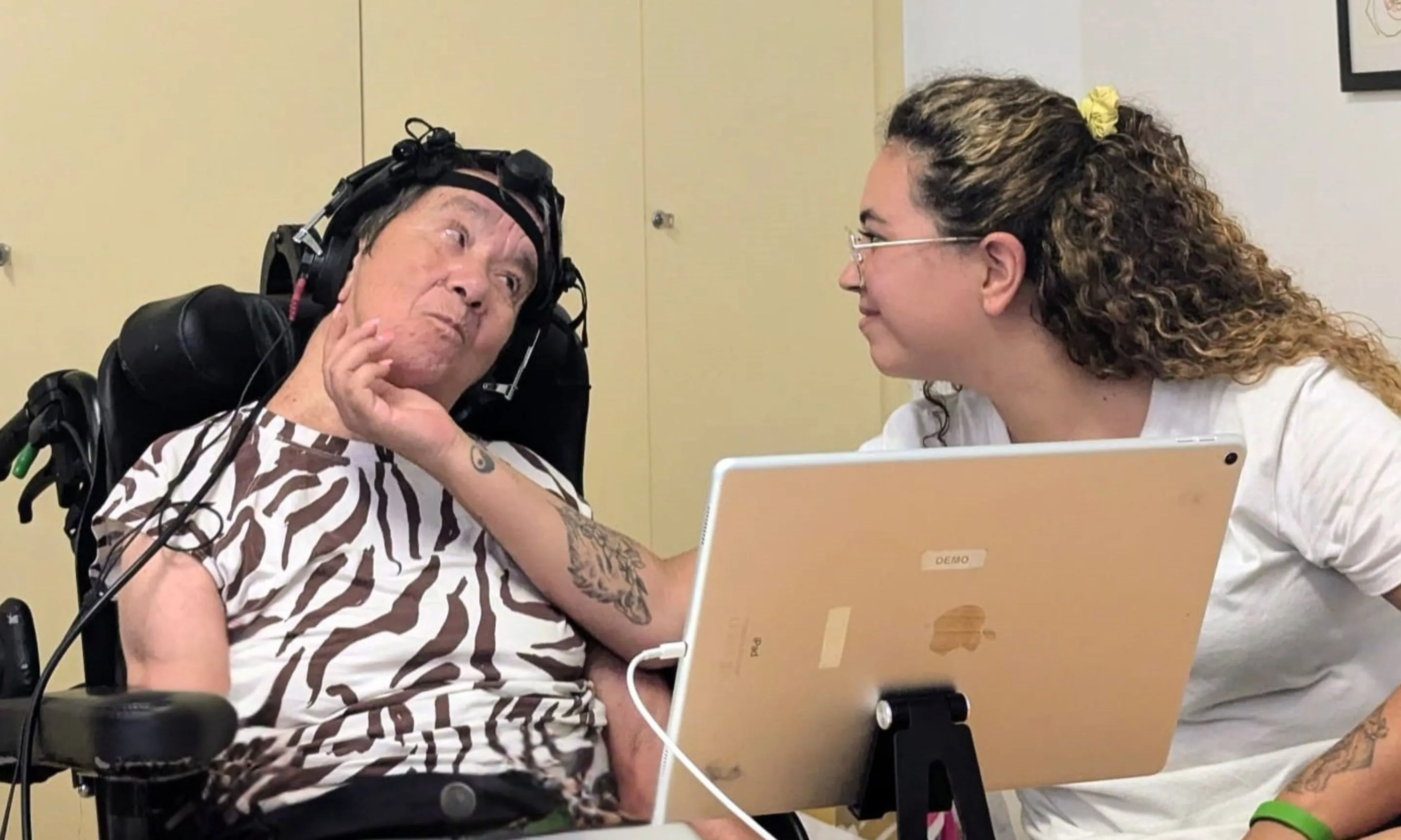 Una professional realitza una prova auditiva amb una persona usuària que porta una diadema amb sensors EEG mentre observa una pantalla.