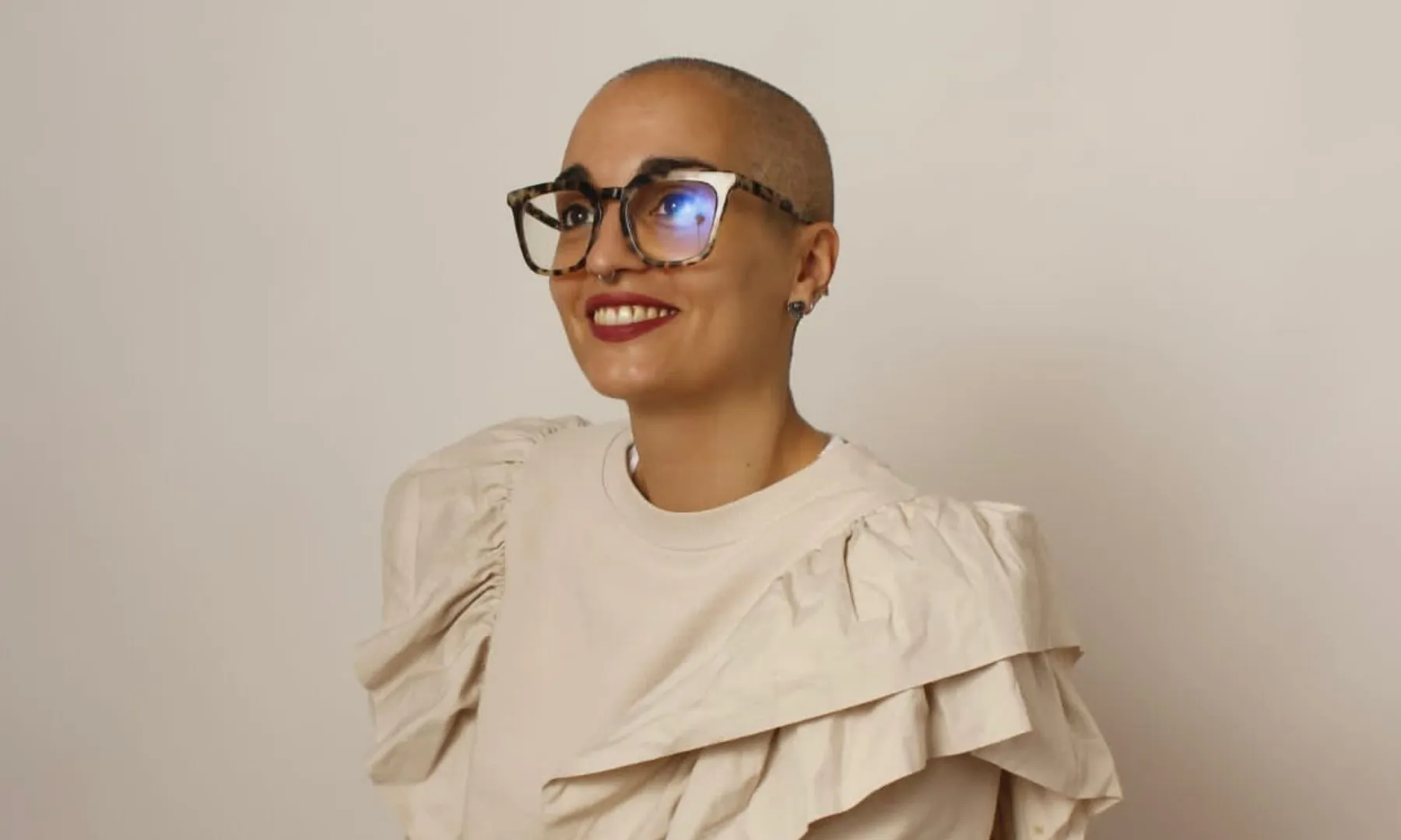 Retrat d’una dona amb alopècia i ulleres somrient sobre fons neutre.