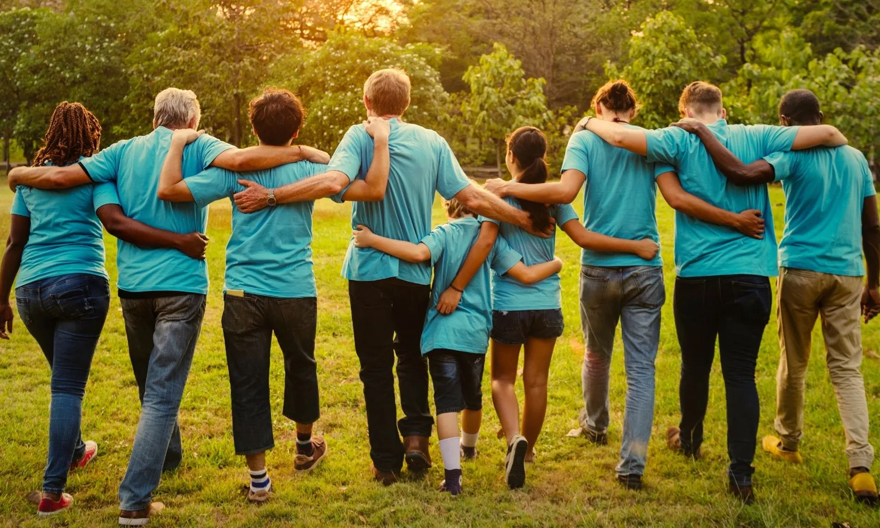 Grup divers de persones caminant abraçades en un espai natural, representant cohesió social, suport mutu i comunitat.