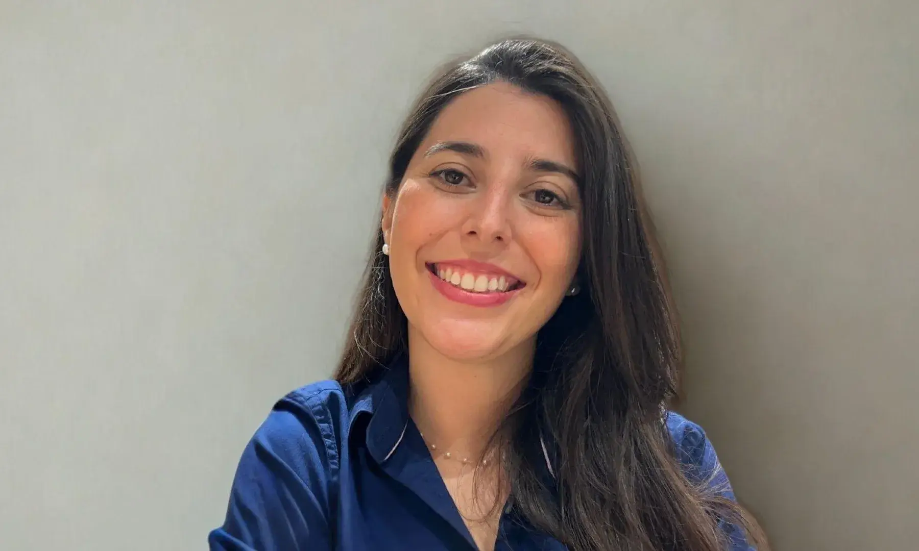 Dona jove amb cabell llarg castany i camisa blava somriu mirant a càmera davant d’un fons clar.