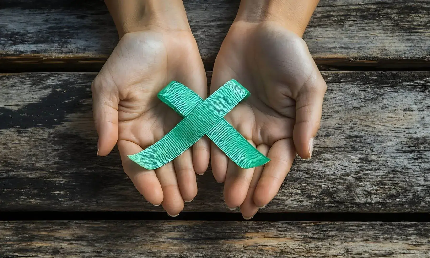 Dues mans obertes sostenen una cinta verda en forma de X sobre una superfície de fusta.