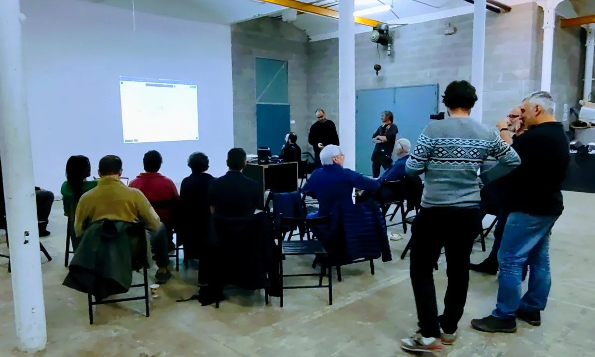 Una trobada d'eXO, amb els seus membres fent una presentació i un grup de gent de públic en cadires.