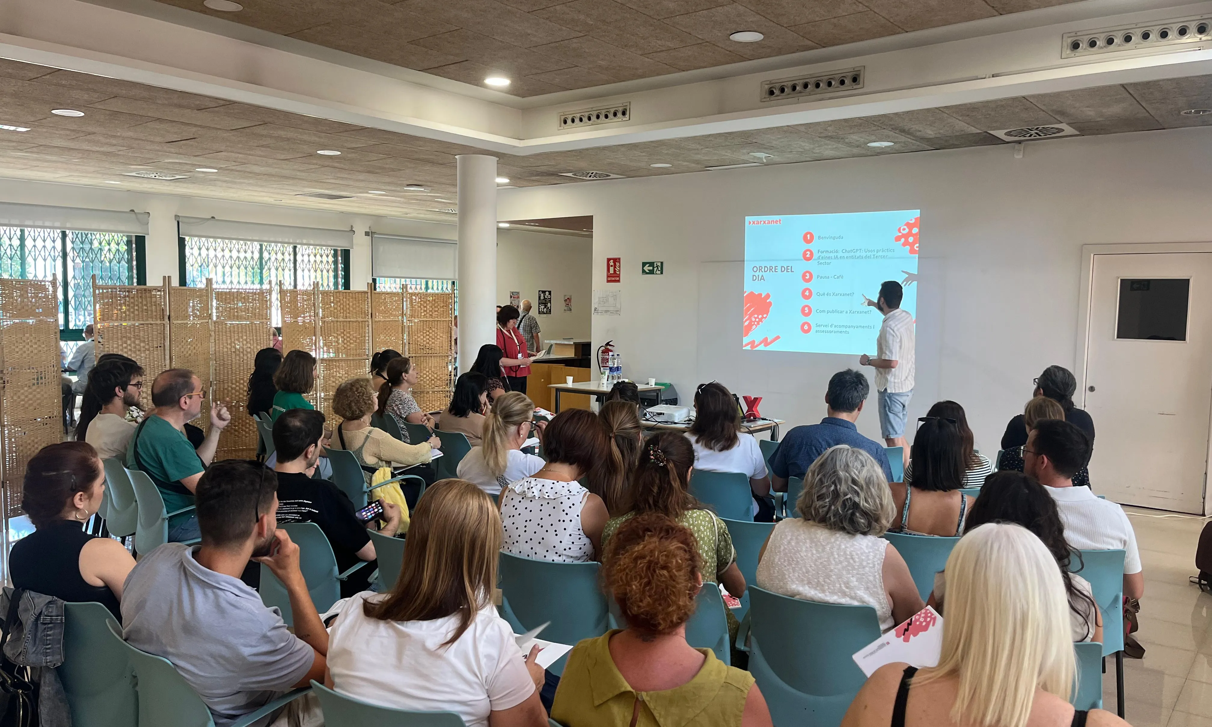 Quatre files de persones observant la presentació d'un noi davant una pantalla.