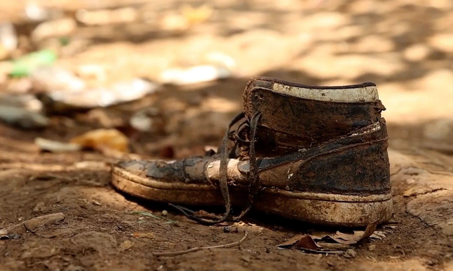 Una sabata plena de fang abandonada enmig d'un camí de terra.