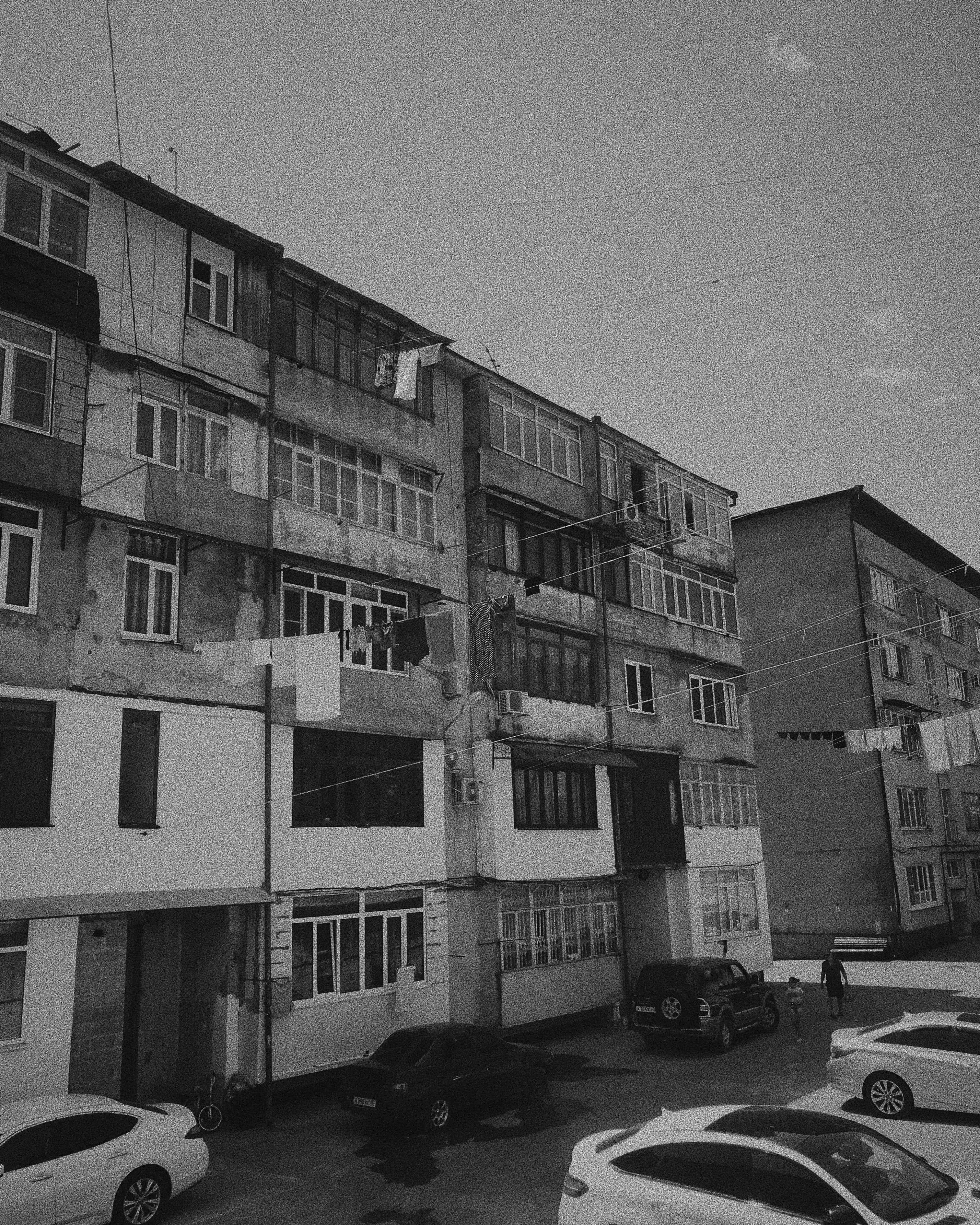 Carrer amb cotxes aparcats de manera aleatòria amb edificis molt senzills de fons