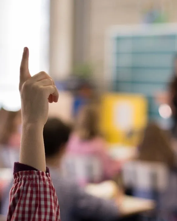 Jornada ‘Repensant l’escola: Què fa? Què haurà de fer?’ Classe on es veu un alume que alça la mà, amb la mestra de fons