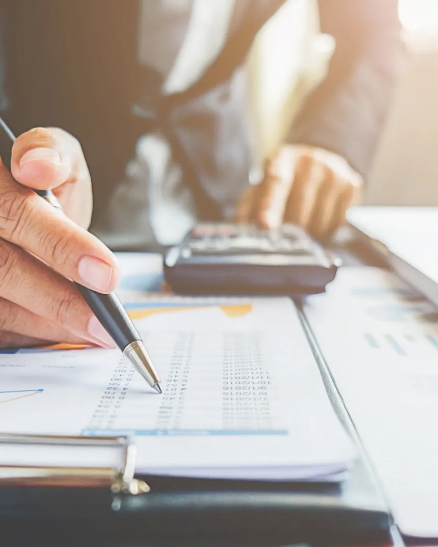 Persona revisant documents financers amb una calculadora i un ordinador portàtil sobre la taula.