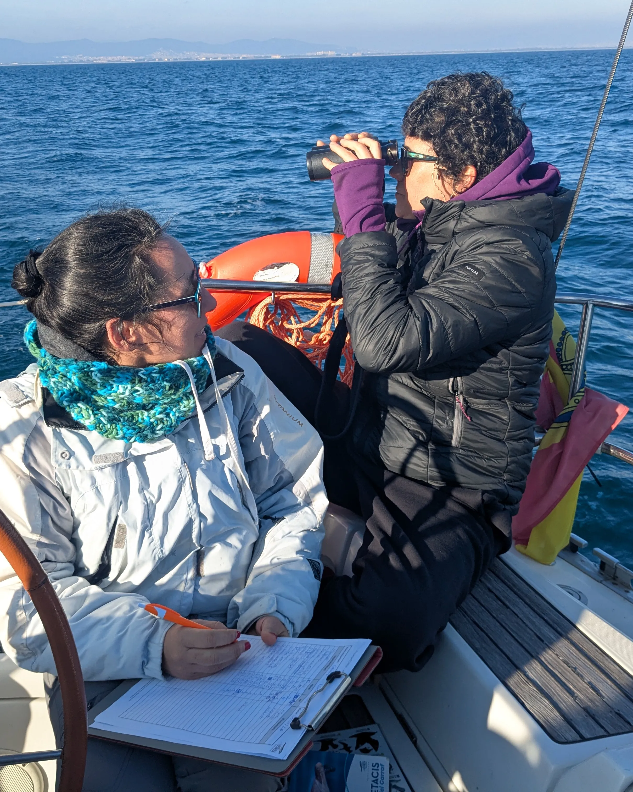 Dues voluntàries en un vaixell al mar, mirant per uns binocles.