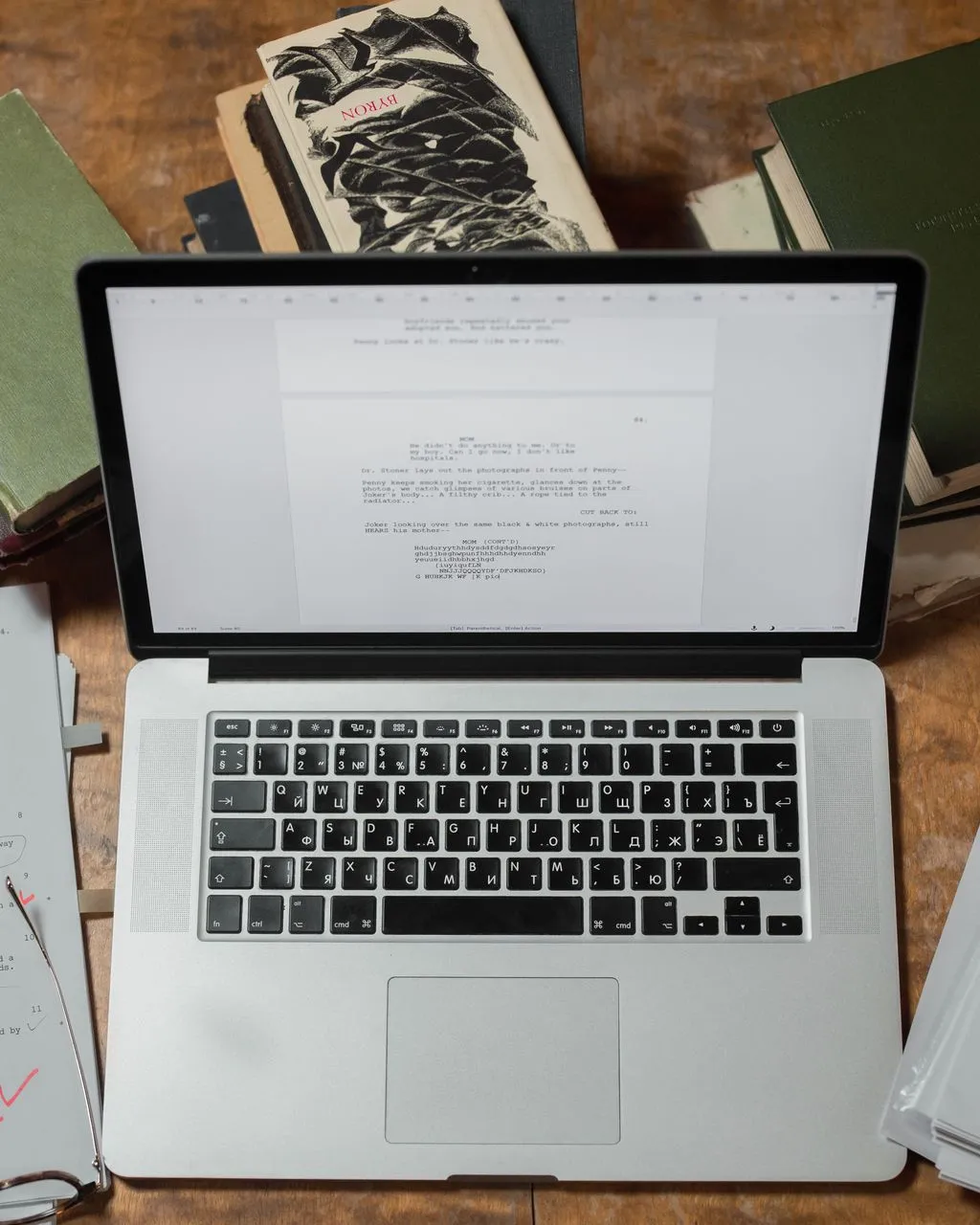 Un portàtil envoltat de llibres i guions sobre un escriptori de fusta.