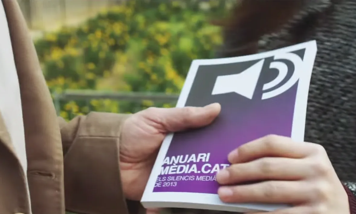 Dues persones es passen l'Anuari dels Silencis Mediàtics 2014.