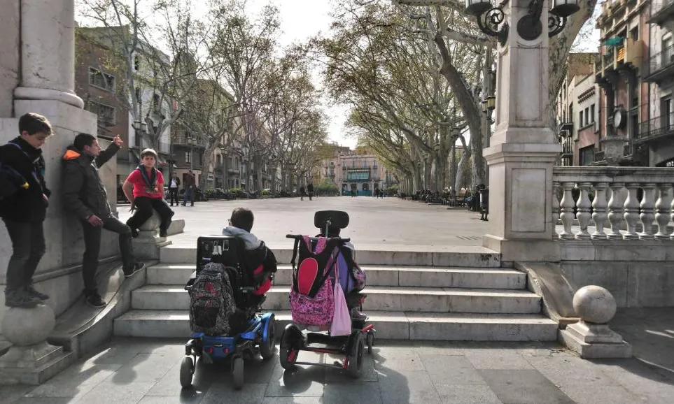 Infants escoltes i joves amb mobilitat reduïda davant l'obstacle d'unes escales.