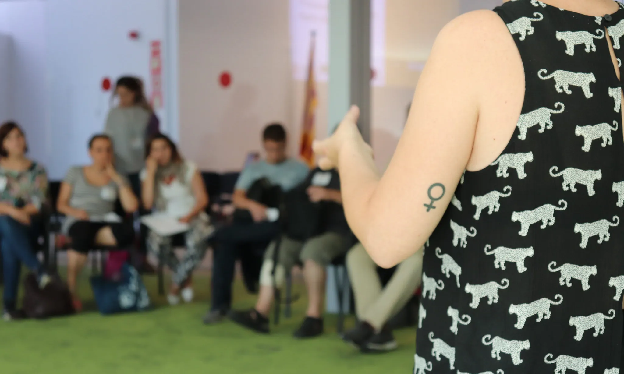 Núria Alonso presentant el taller sobre perspectiva de gènere a la JdIS. En la foto es veuen persones de fons i un braç amb el símbol de les dones tatuat