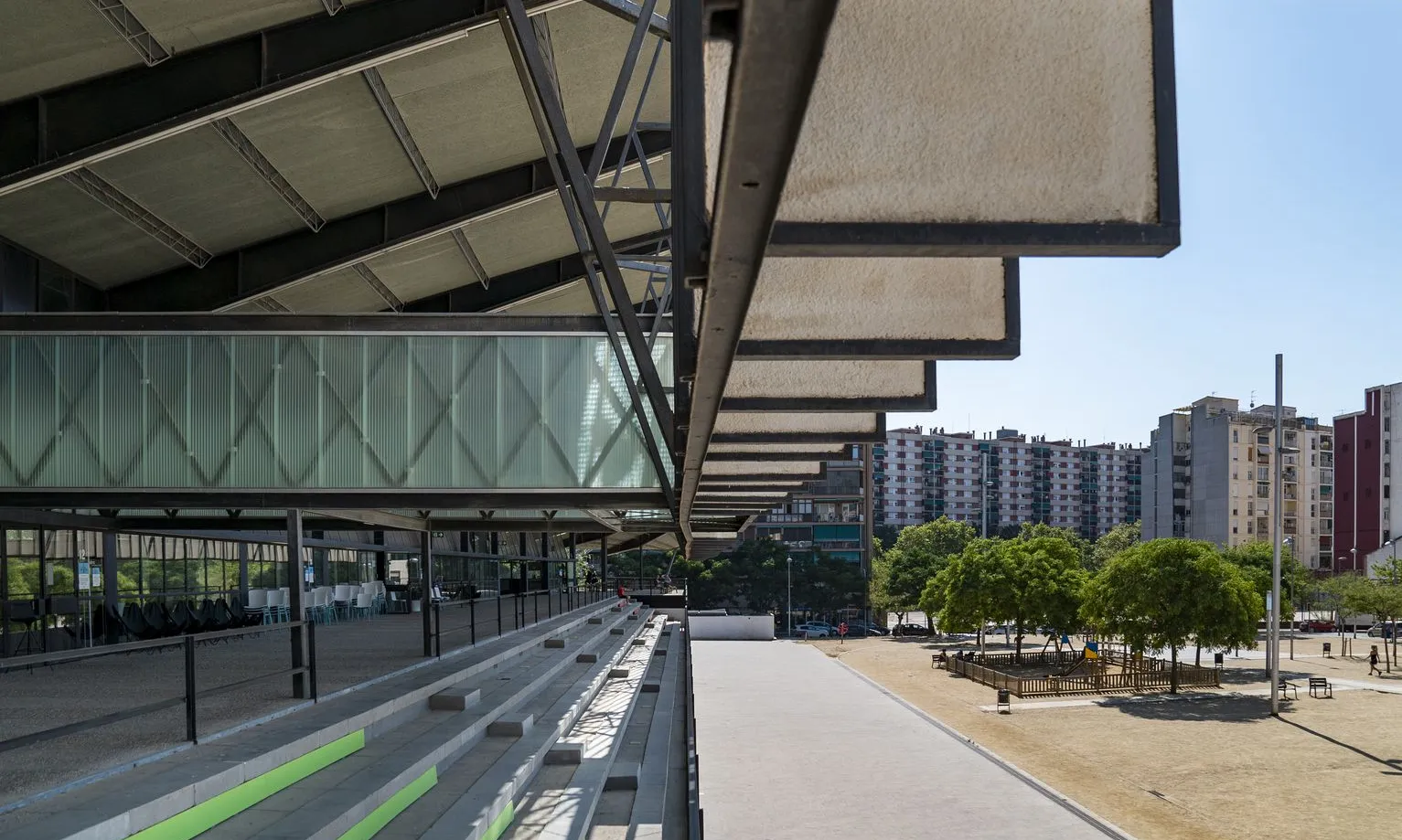 Graderies d’accés a l’edifici del Canòdrom, amb una coberta en voladís que la protegeix del sol i on la gent seu. 