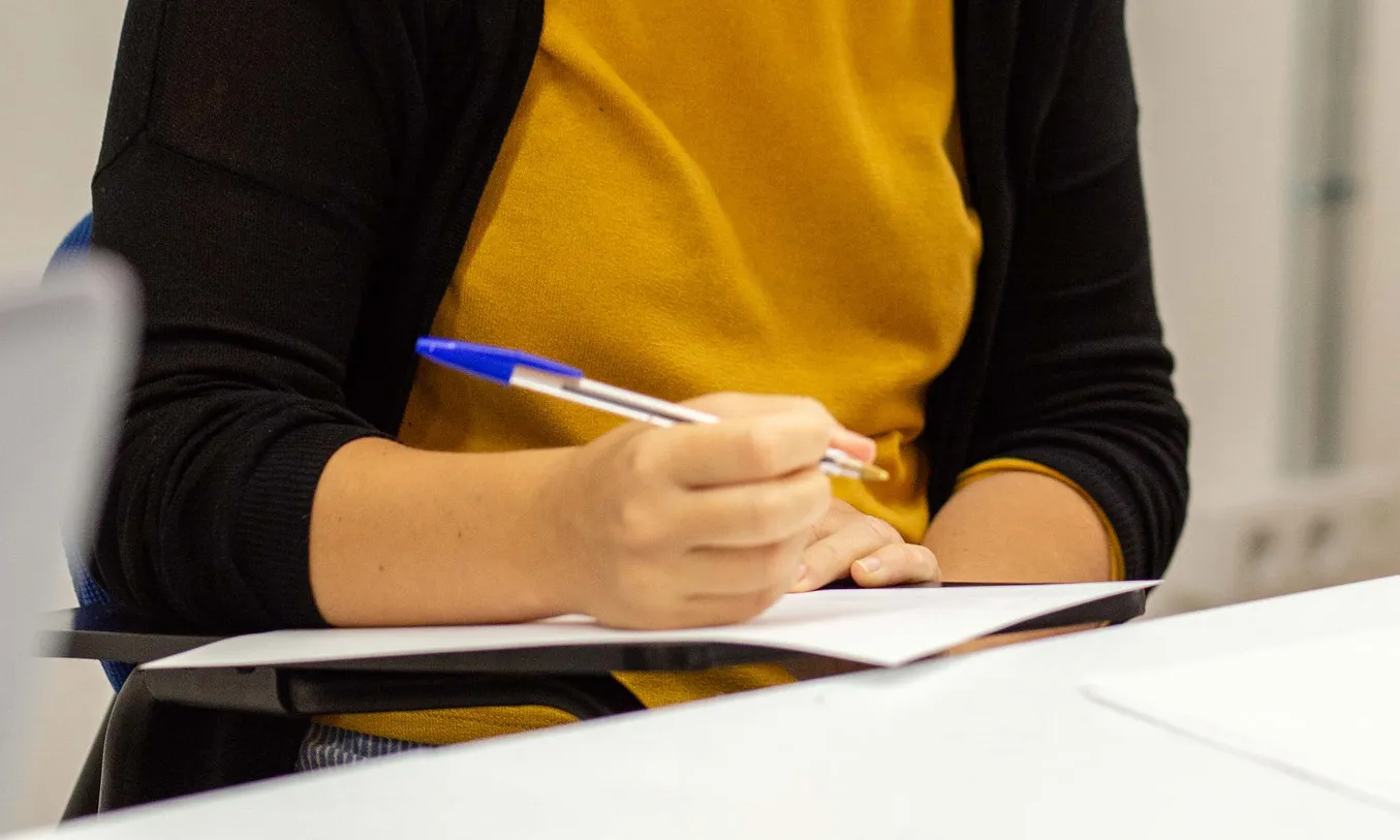 Pla detall de les mans d'una dona escrivint en un entorn de treball.