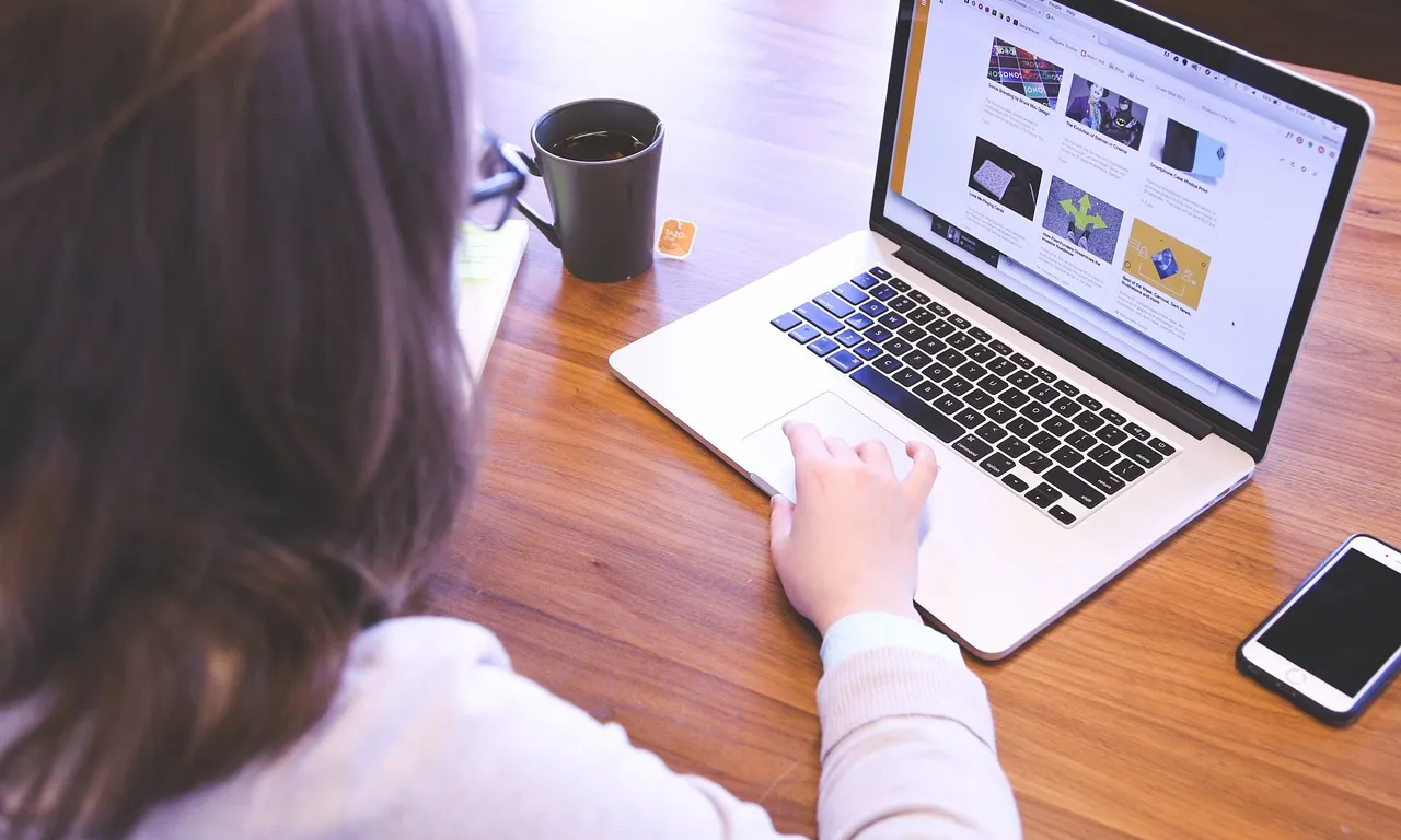 Persona treballant amb un ordinador portàtil i amb un café sobre la taula