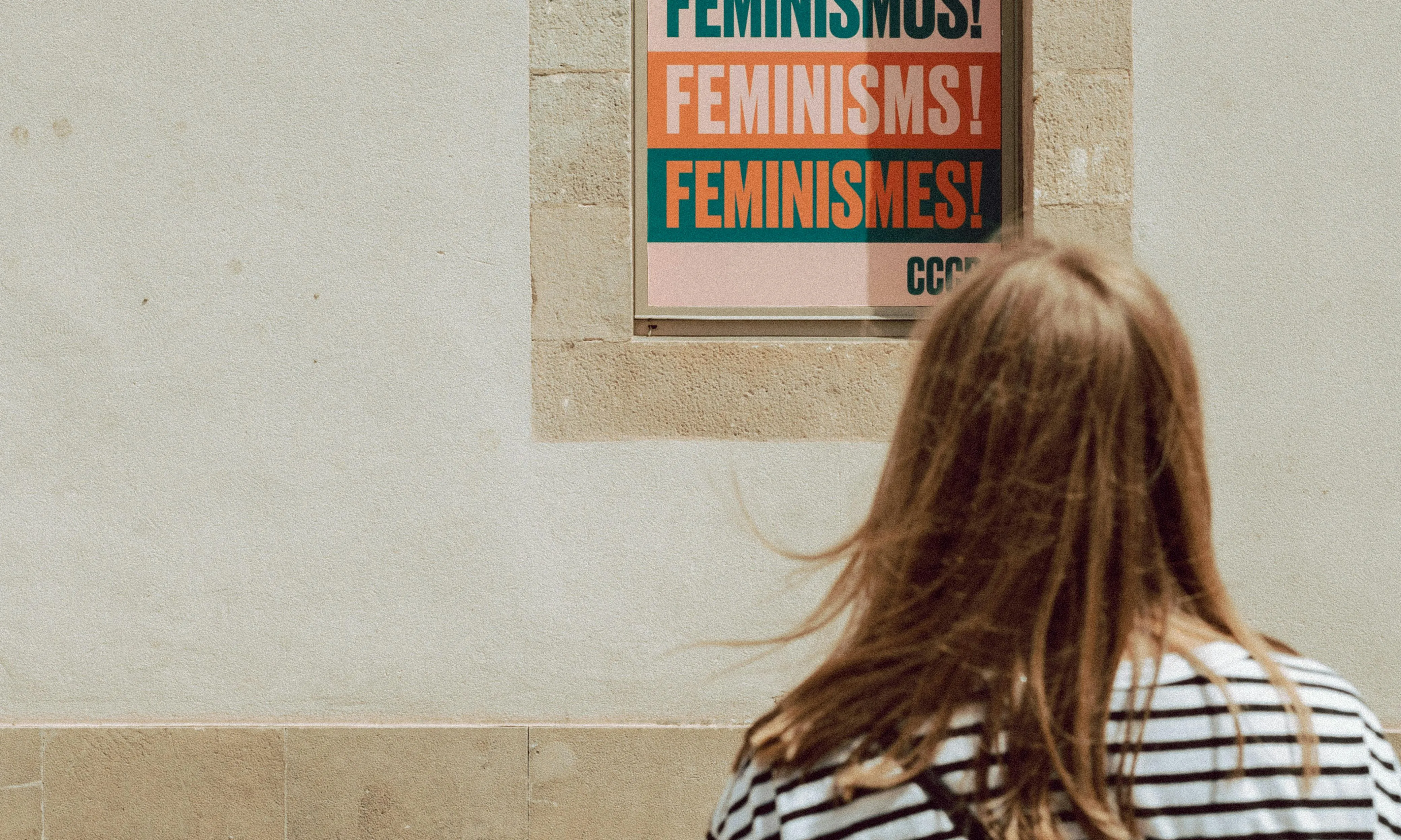 Noia mirant un cartell on posa feminisme en diferents idiomes. Font: Pexels - Sinitta Leunen
