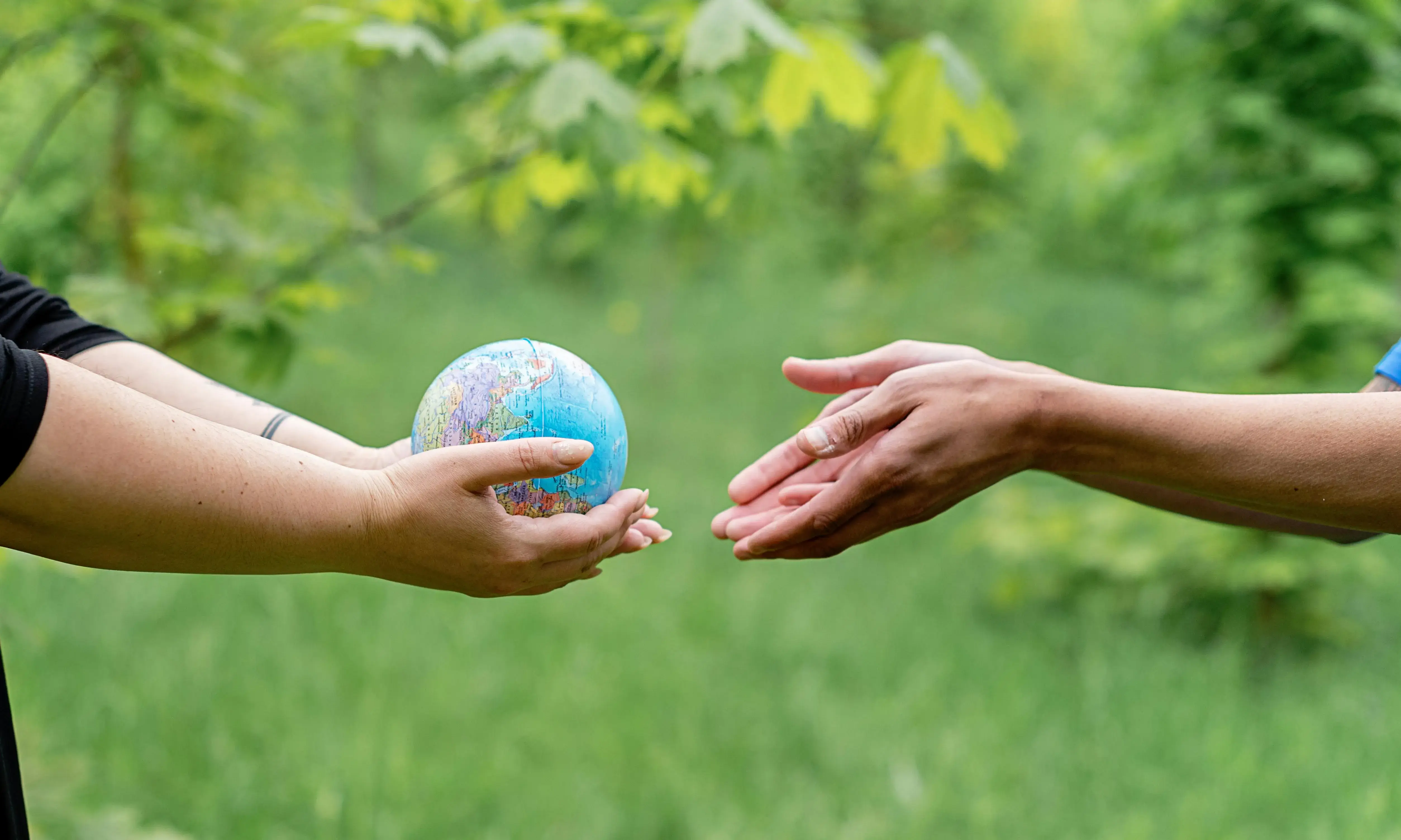 Cooperació internacional Dus persones amb braços estesos que es passen un globus terraqui
