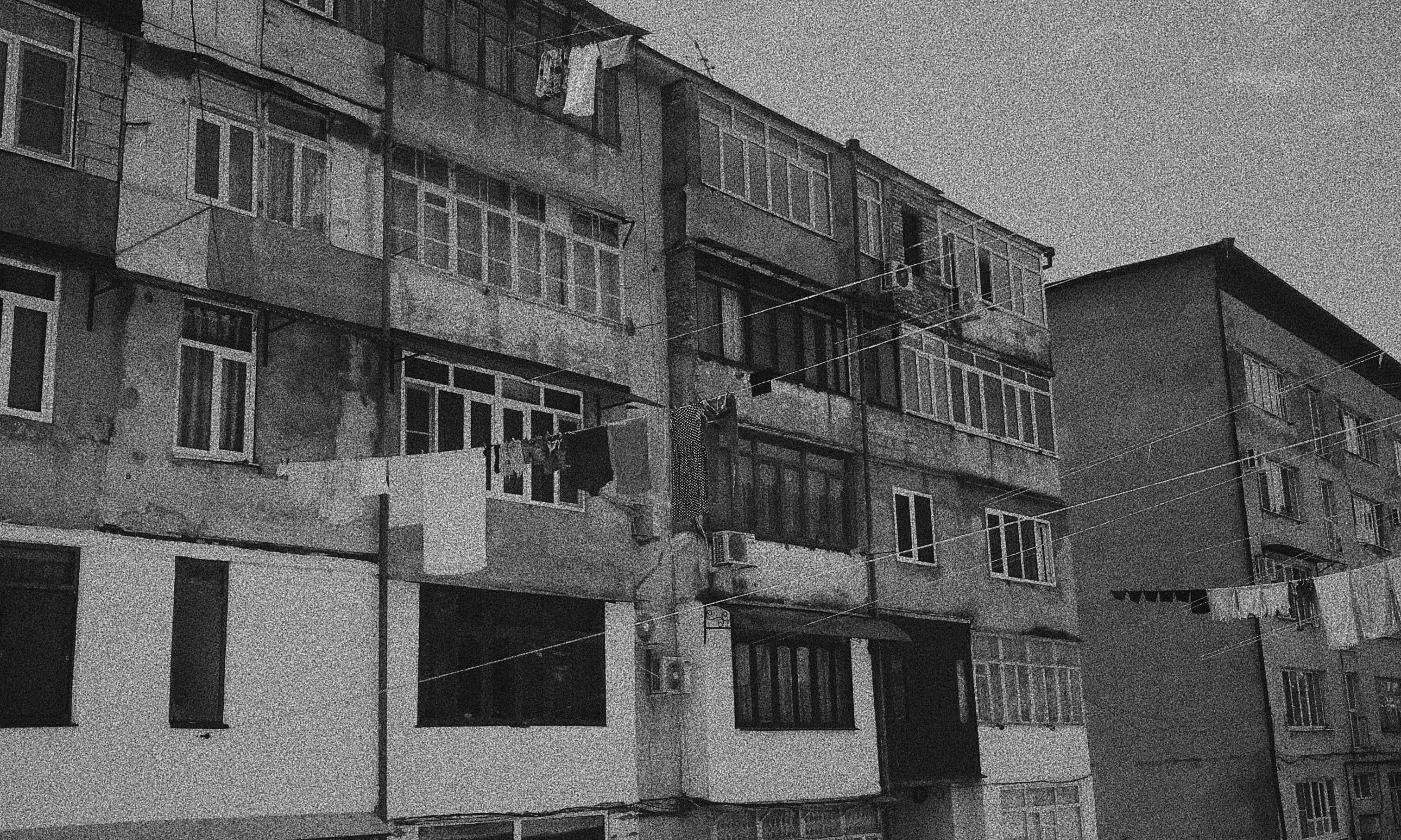 Carrer amb cotxes aparcats de manera aleatòria amb edificis molt senzills de fons