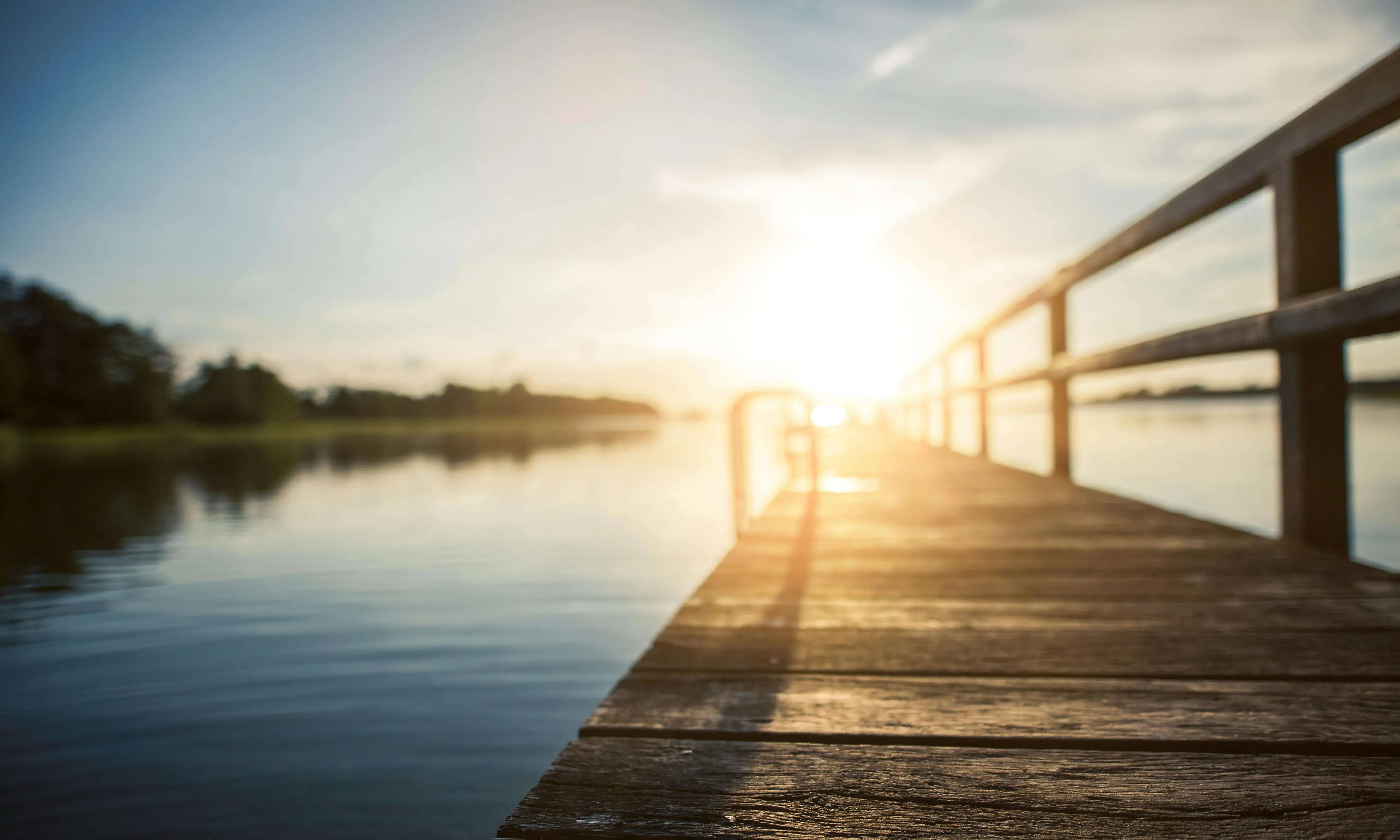 Llac amb passarel·la i posta de sol al fons