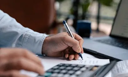 Economia Persona amb una calculadora apuntant dades en un full