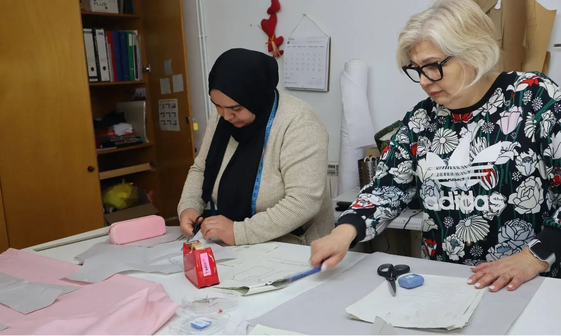 Dues dones confeccionen roba de color rosa.