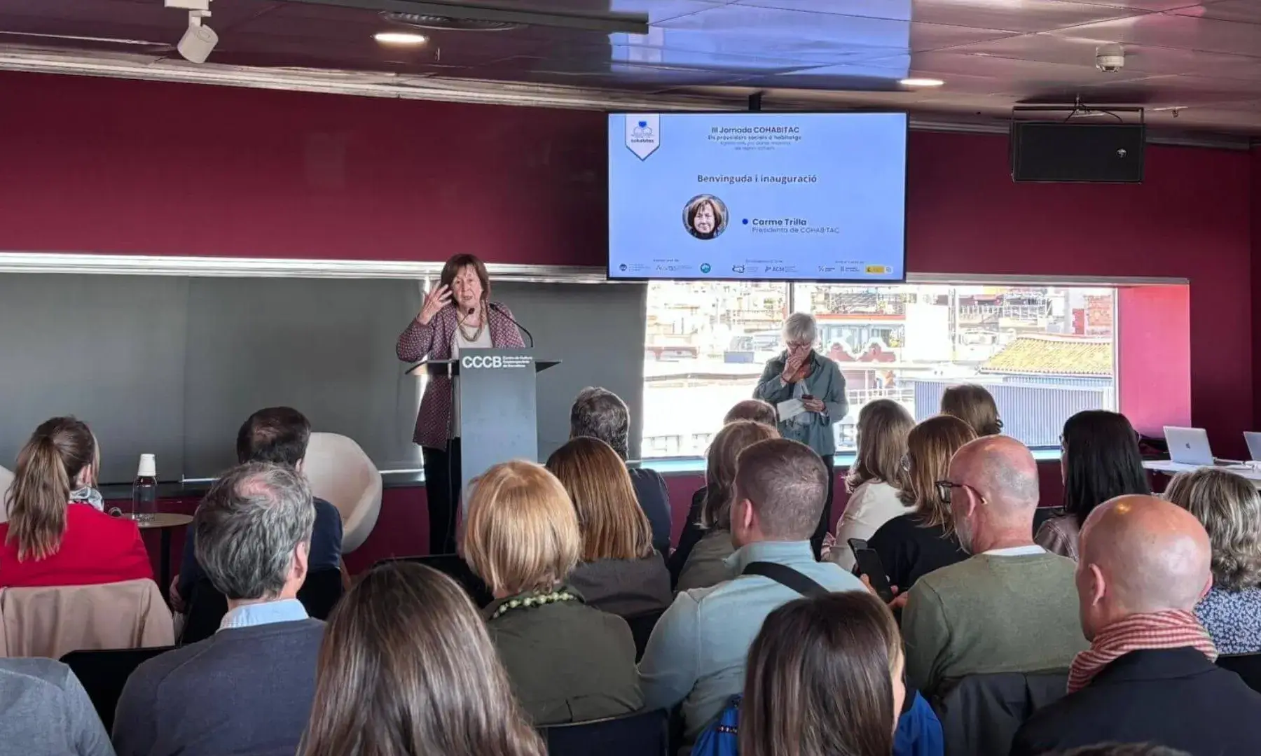 Carme Trilla intervenint durant la inauguració de la III Jornada COHABITAC al CCCB davant d’una sala plena de públic.