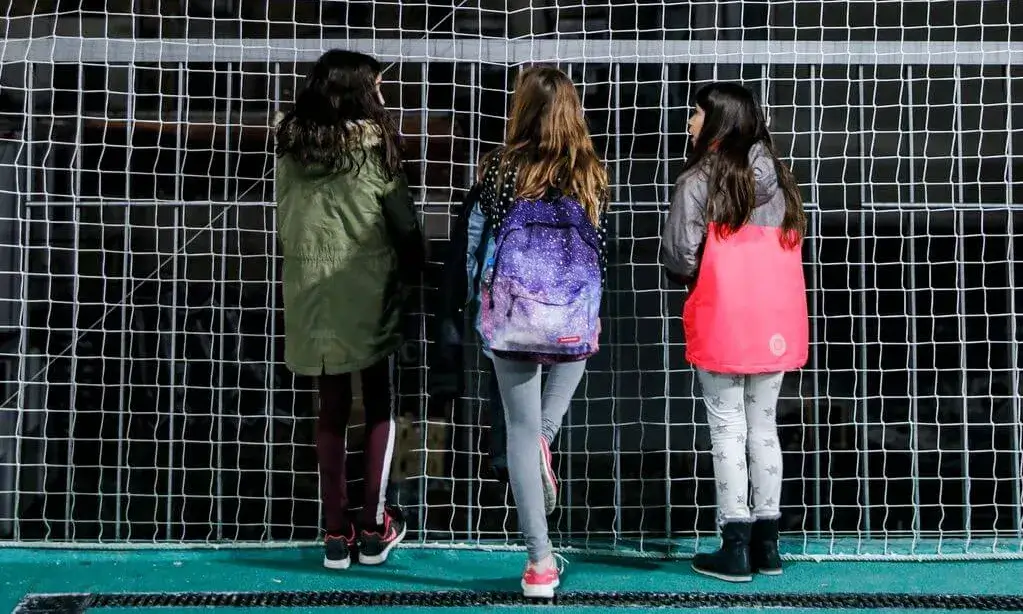 Nenes en un pati d'escola en front d'una xarxa.